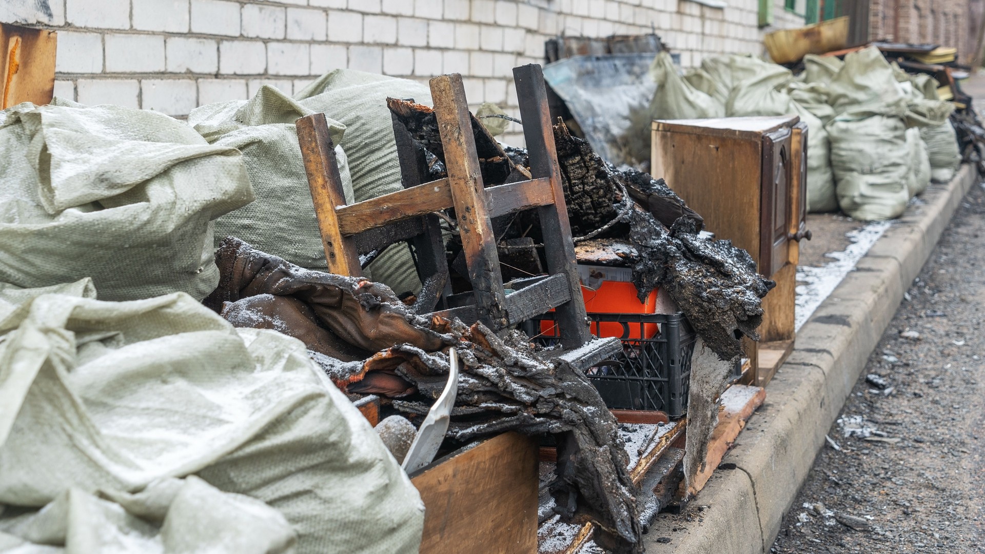 A private home stands in ruins after a devastating fire, with charred belongings scattered on the street. The scene reflects the aftermath of destruction and loss, evoking deep emotions.