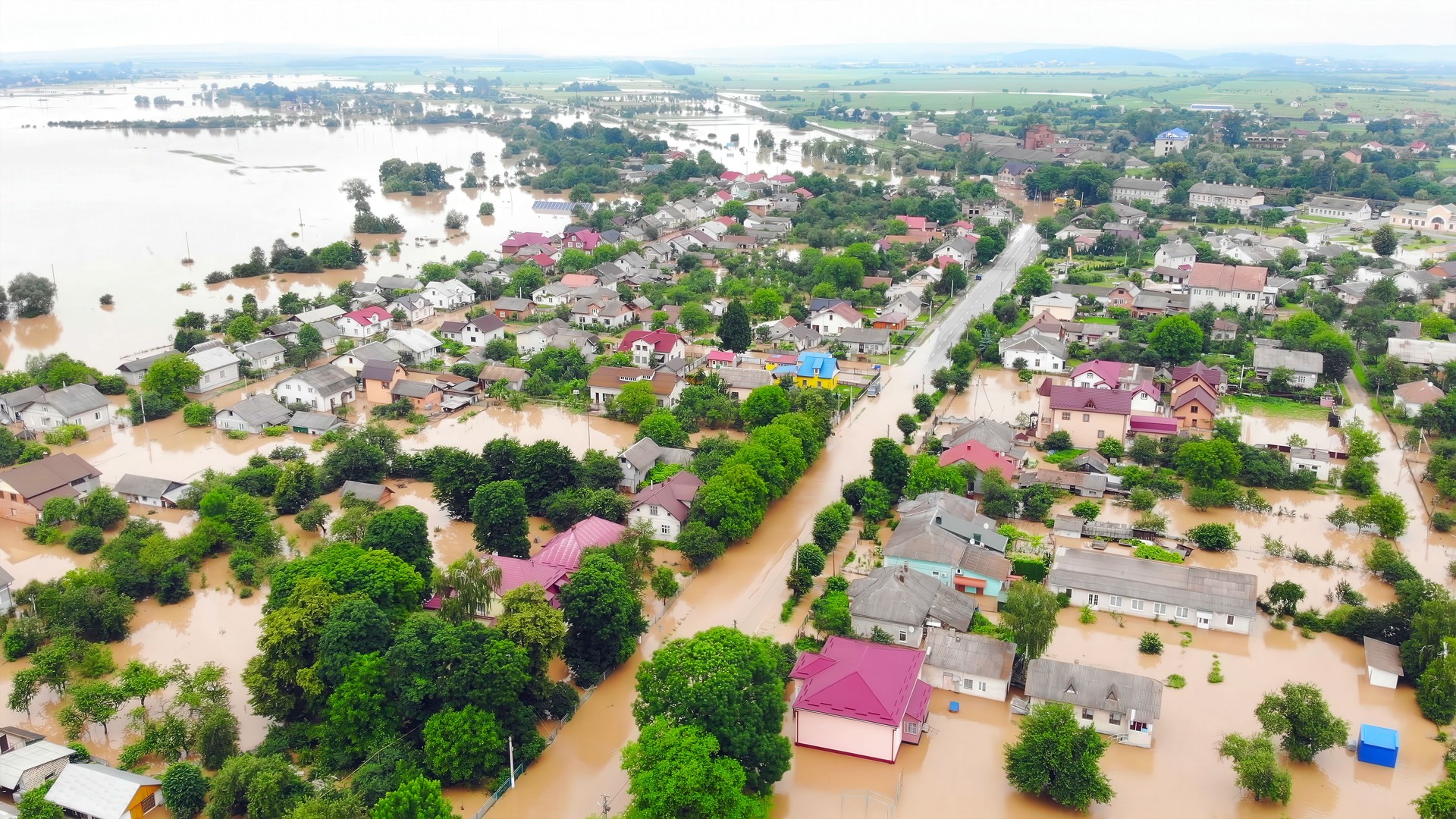 Aerial view of flooded residential area. Wide aerial view of a town submerged in floodwater after heavy rainfall, showing houses, streets, and surrounding landscape affected.